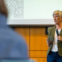 woman holding microphone presenting to full room